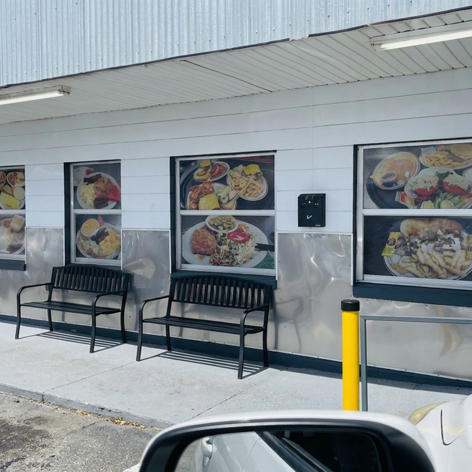 Restaurant exterior with food photographs displayed in windows, two black benches, and a covered sidewalk entrance.