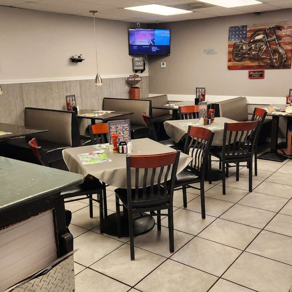 Casual restaurant dining room with neatly set tables, booths, motorcycle décor, counter, and one seated diner.