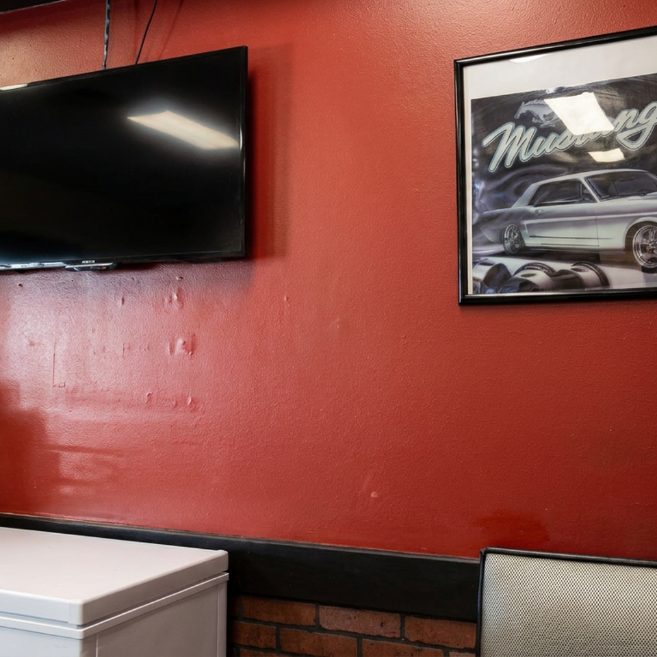 Restaurant interior with red walls, a wall-mounted television, classic Mustang poster, coffee mug display, and white chest freezer.